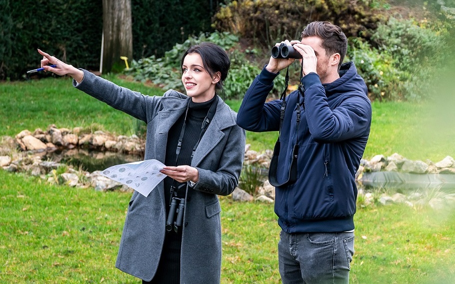 Deux personnes se rencontrent pour observer les oiseaux. L'homme regarde &agrave; travers des jumelles, tandis que la femme montre quelque chose du doigt.